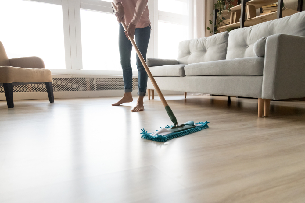 Woman mopping floors in a living room while performing floor care.